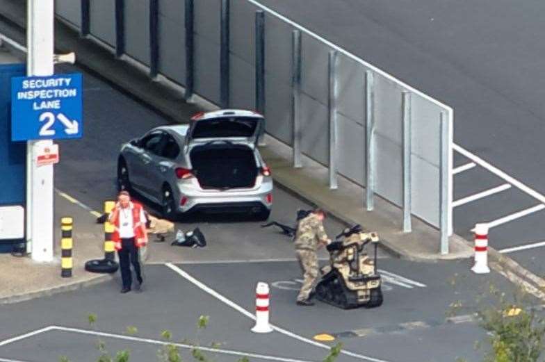 An Army explosive expert operates a specialist bomb disposal robot to search a silver car in a security lane. Pic: UKNIP