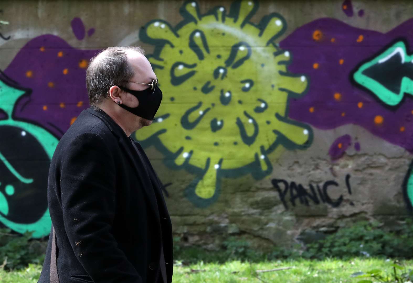 A man wearing a mask walks past coronavirus-related graffiti in Edinburgh (Andrew Milligan/PA)