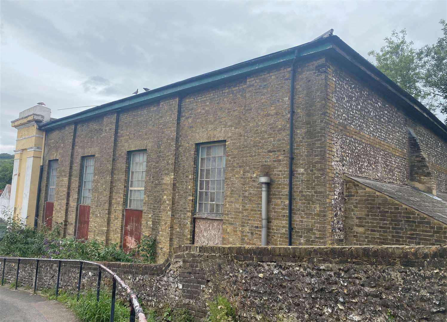 The building, as seen from behind, is surrounded by overgrown weeds