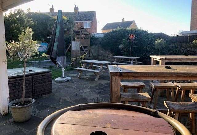 The patio area of the garden has several tall, chunky wooden tables and high stools