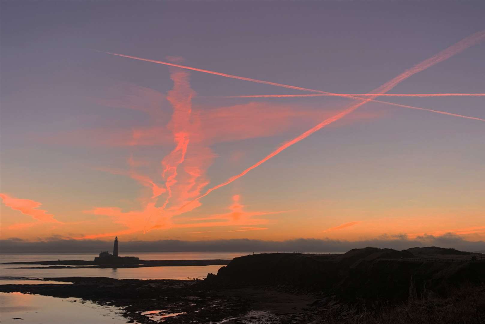 Plane contrails lit by the sun below the horizon before sunrise at St Marys Lighthouse in Whitley Bay off the North East coast (Owen Humphreys/PA)