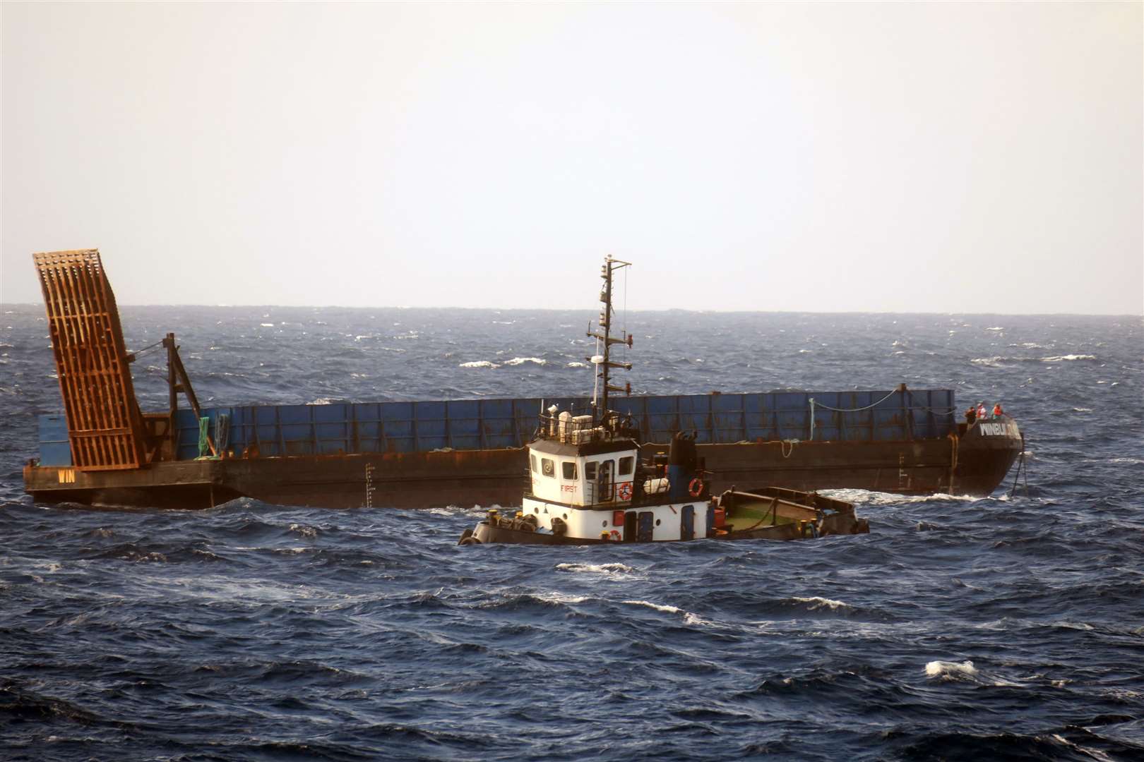 The stricken tug with the crew huddled on the bow of the sand barge it was towing. Photo: Royal Navy