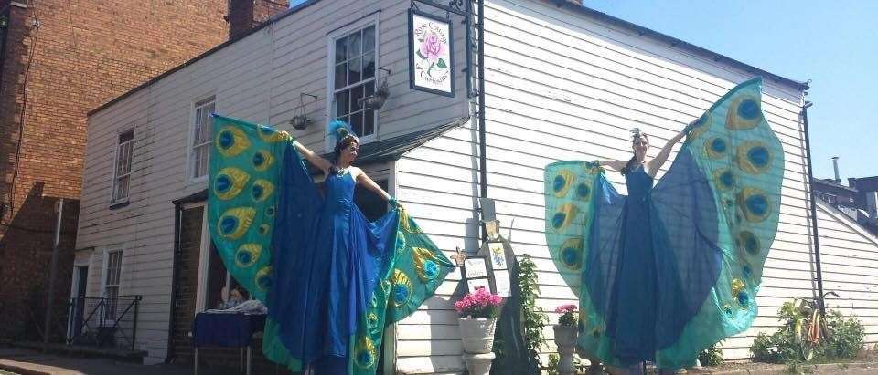 Stilt-walking 'peacocks' in front of the distinctive white weather-boarding of the Cottage of Curiosities in Rose Street, Sheerness