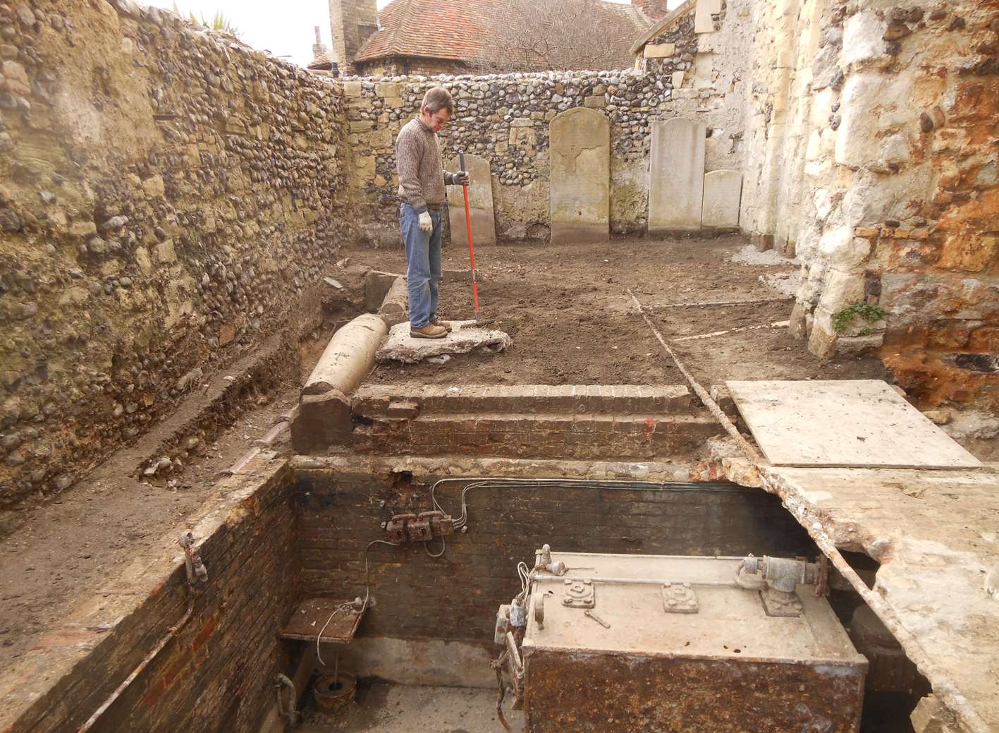 Volunteer digger Gareth inspects the 20th century heating plant which has been left exposed and will be removed allowing space to construct toilets