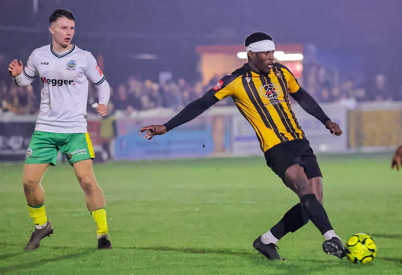 Folkestone defender Marvel Ekpiteta - bandaged up in Terry Butcher style - gets away from Dover's Harrison Pont. Picture: Helen Cooper