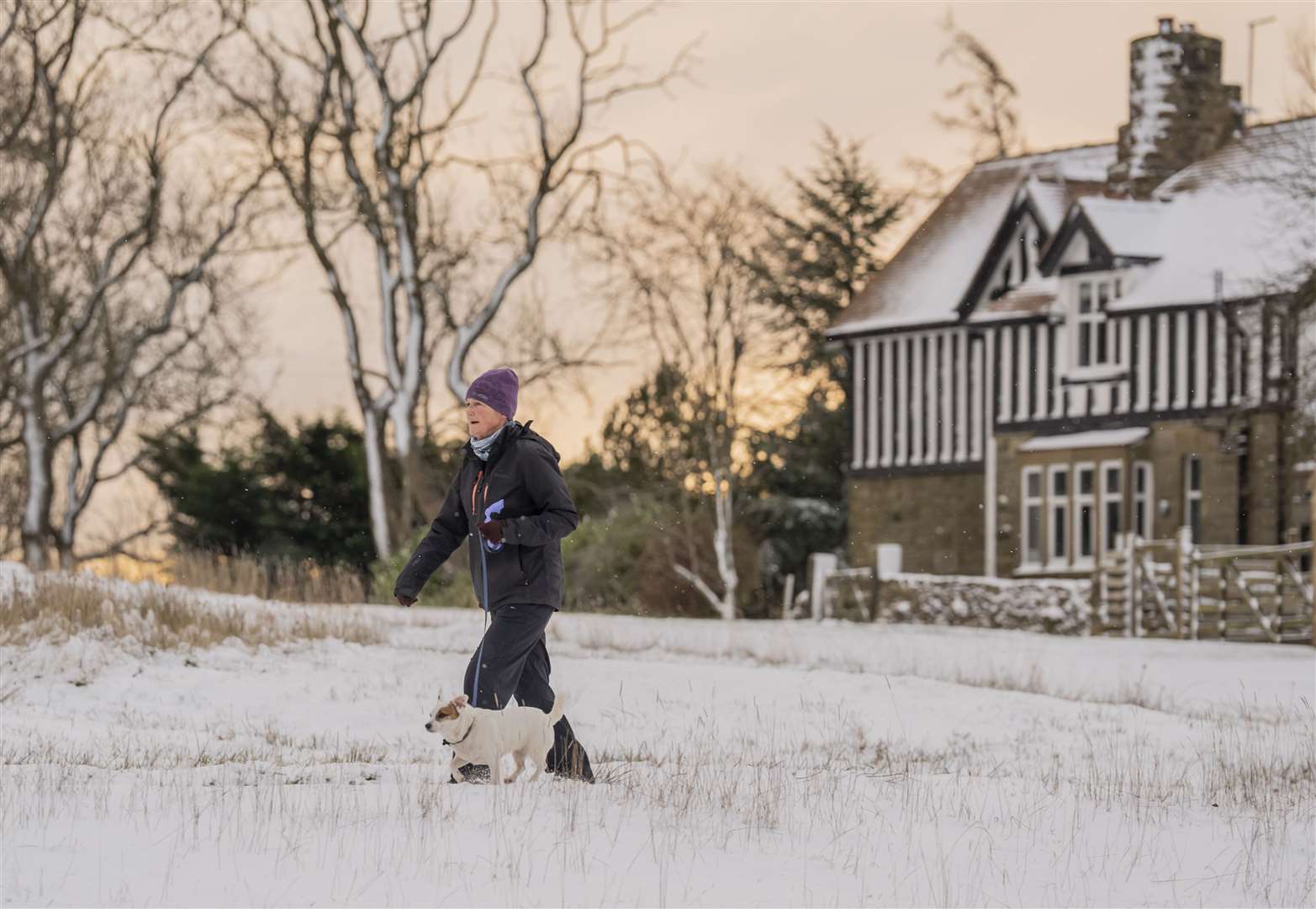 A woman walks her dog in fresh snow in Goathland (Danny Lawson/PA)