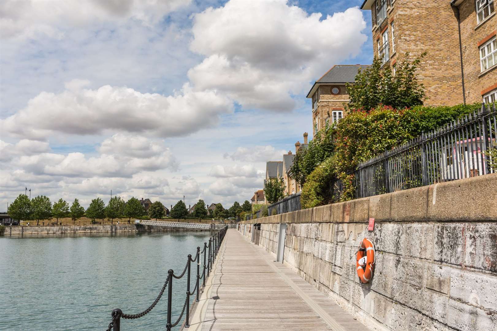 These houses are on the side of a dock and have a boardwalk footpath in front of them accessed by a footbridge