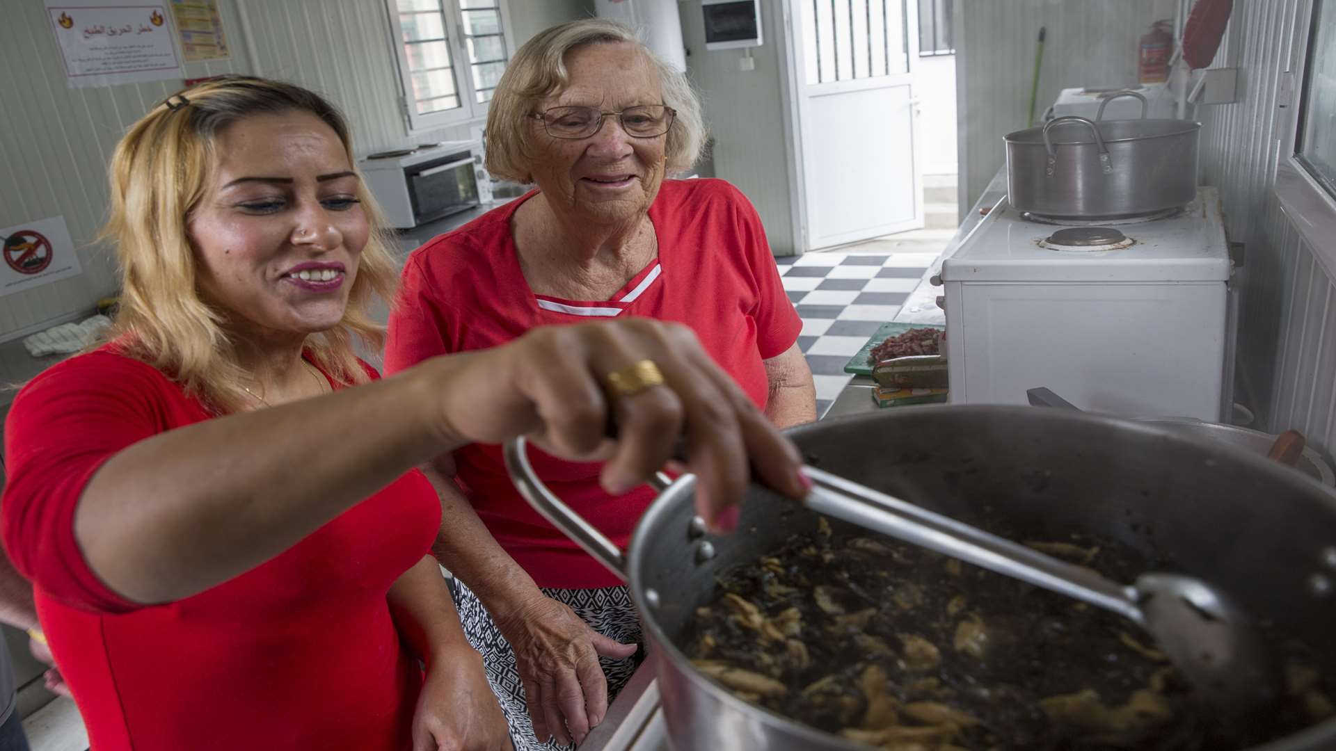 Ramzia, 38, who is from Syria, shows Margot the lunch she is cooking in one of the communal kitchens Oxfam has installed in the Doliana Refugee & Migrant camp in Greece