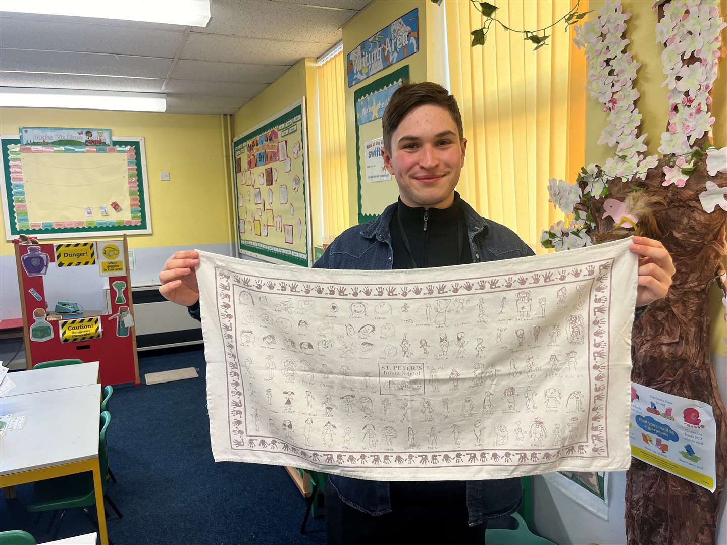 Teacher at St Peter's Infant School, Reo Mardell, holding a tea towel from 2007 with his self-portrait on