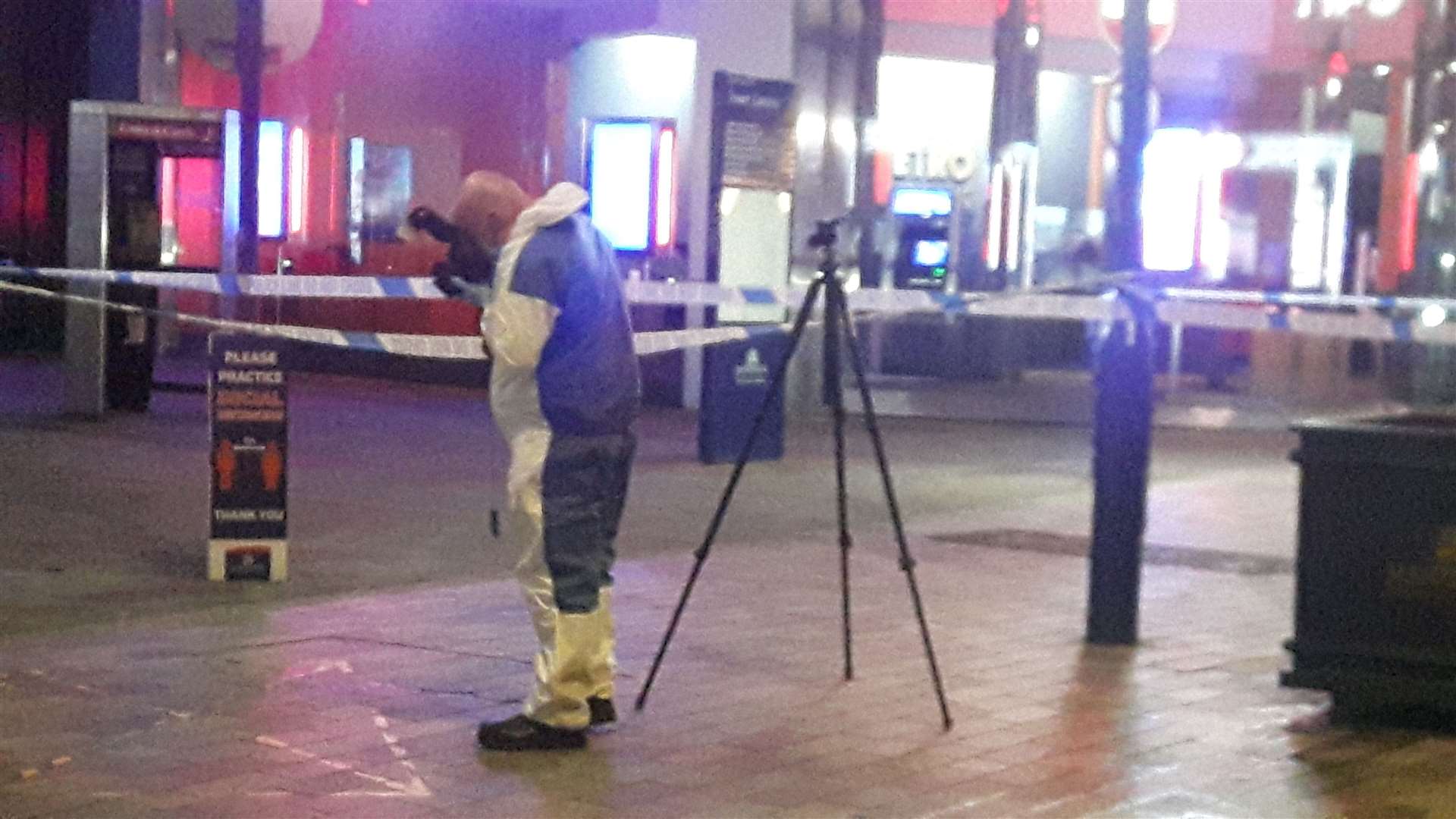 A forensic officer sets up a camera on the corner of Week Street and High Street