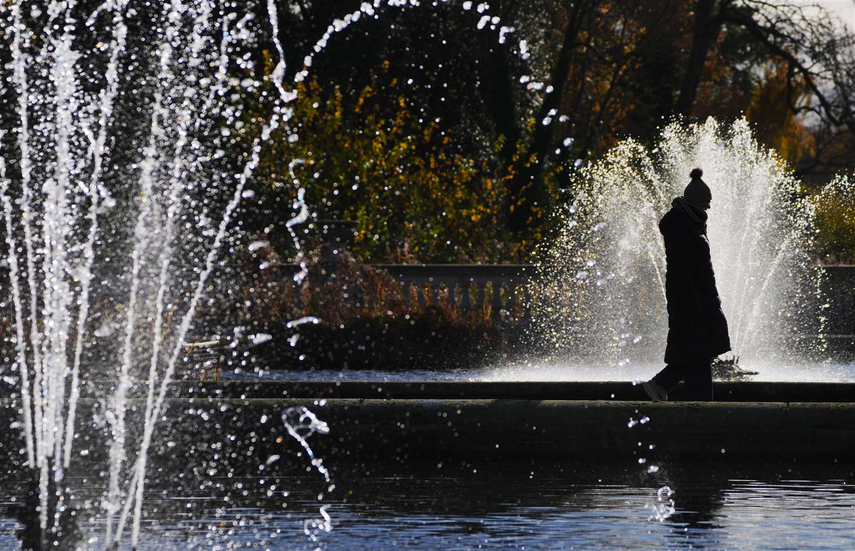 A bundled-up visitor walks between fountains in Hyde Park, London (Jonathan Brady/PA)