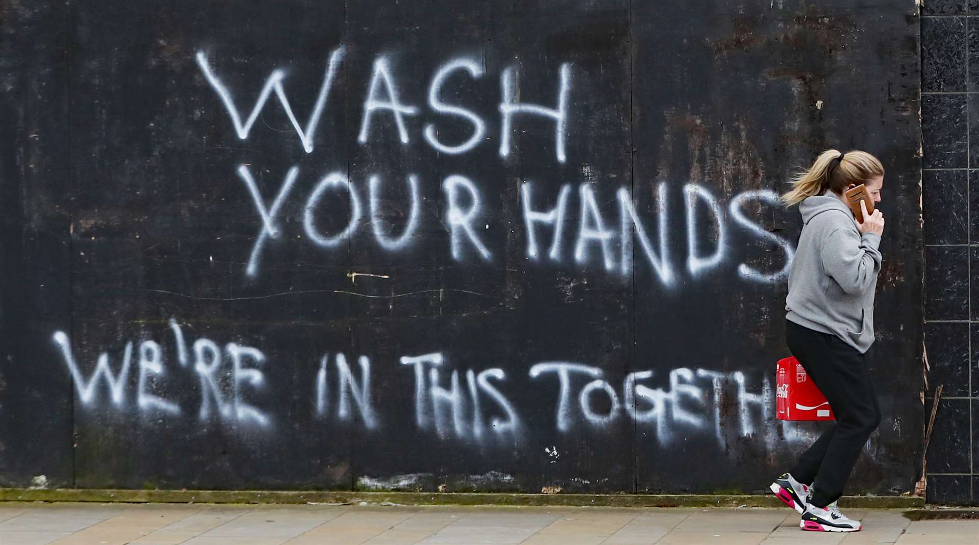 A woman walks past graffiti calling on people to wash their hands during the Covid-19 crisis in east Belfast (Niall Carson/PA)