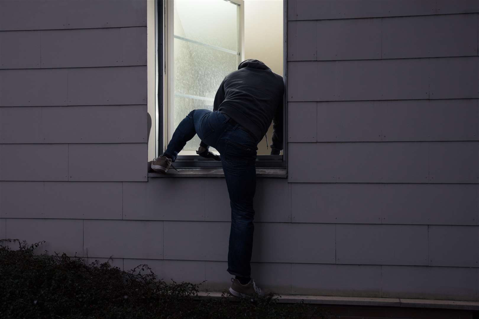 Burglar entering in a house through a window. Stock pic.