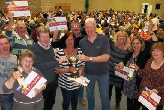 Victorious Moomins captain Janet Cooper receives the Canterbury KM Big Quiz trophy from event sponsors Nick Fairweather of Fairweather Solicitors and Richard Kreffer of MHA MacIntyre Hudson, cheered on by team members.