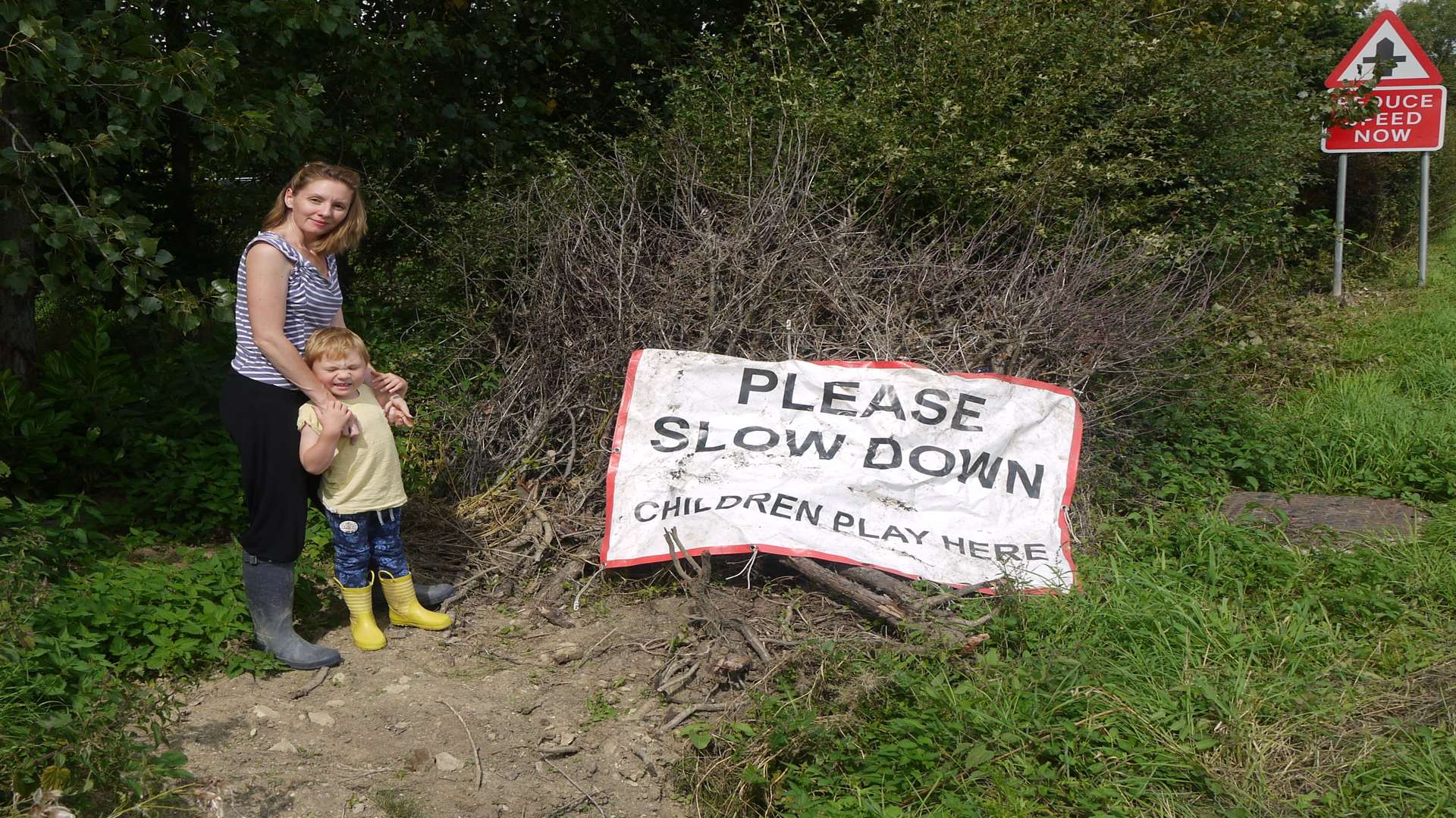 Sally and her son stand near the sign calling for drivers to slow down