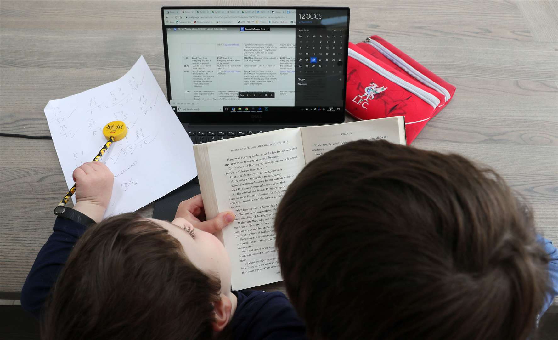 A boy in Dublin reads to his younger brother as his home-schooling timetable suggests noon is Drop Everything And Read time (Brian Lawless/PA)