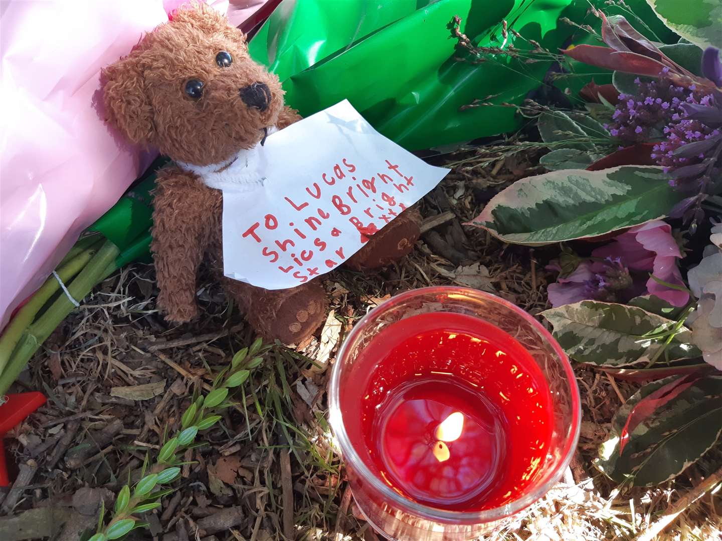 A child leaves a handwritten note attached to a brown teddy bear